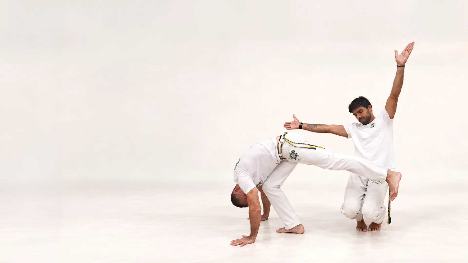 Un capoeiriste en appui au sol passe la jambe au-dessus de son partenaire agenouillé